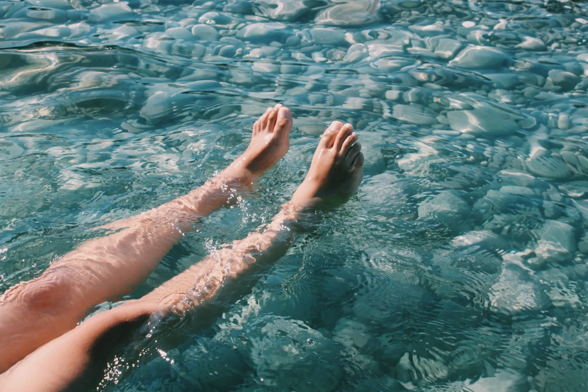 Bare feet lifted above clear, shallow water over smooth stones